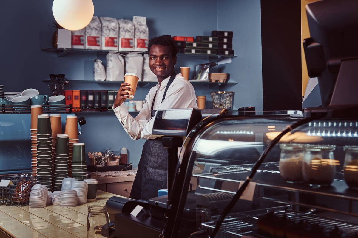 smiling-handsome-african barista standing in-his-coffee-shop